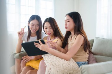 Üç Asyalı kadın dijital tablet ekrana odaklanmış, atıştırmalıklar ve sıcak havayla birlikte serin bir film anının tadını çıkarıyorlar..