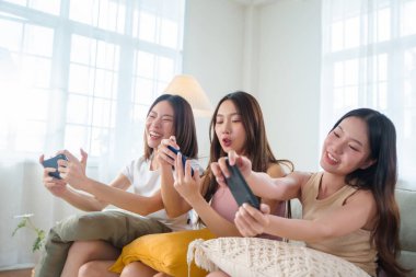 Üç genç Asyalı kadın, oturma odasındaki akıllı telefonlarıyla grup oyun oturumunun keyfini çıkarırken gülüşmelerini paylaşıyorlar..