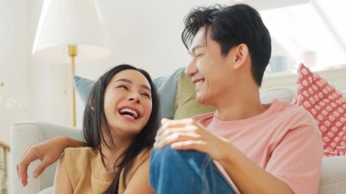 Genç Asyalı çift beyaz koltukta oturmuş gülümsüyor ve muhabbet ediyor. İlişki ve mutluluk kavramı.