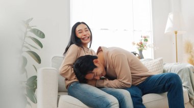 Genç Asyalı çift hamilelik testine neşeyle tepki veriyor, kadın gülümserken erkek duygusal olarak kucağına yaslanıyor..