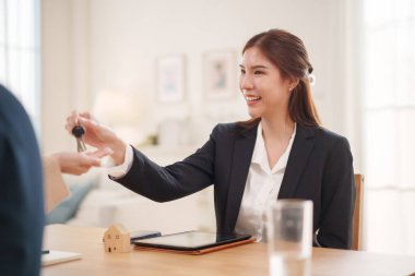 Asyalı kadın ajan, emlak alım satımı sırasında ev anahtarını verirken gülümsüyor ve başarılı bir anlaşmayı kutluyor..