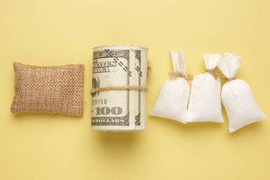 A picture of roll fake money with 3 flour bag and wheat bag on yellow background. Food trading and supply concept.