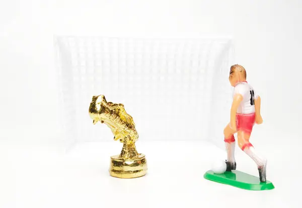 A miniature of golden boot with football player diorama with goal insight on white background.