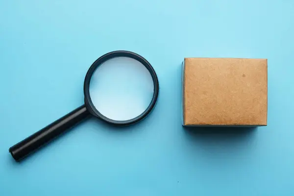 A picture of magnifying glass with carton box on blue background. Search the item.