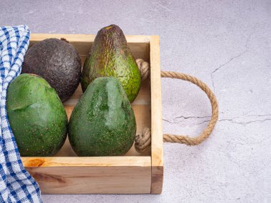 Avocados are placed in a wooden crate on a gray stone background. Space for text. Close-up photo. Concept of healthy fruits.