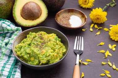 Ev yapımı guacamole, avokado, limon, tuz ve biber gibi malzemelerle birlikte koyu taştan bir arka plana yerleştirilmiş taze guacamole. Üst Manzara. Geleneksel Meksika hazırlığı kavramı.