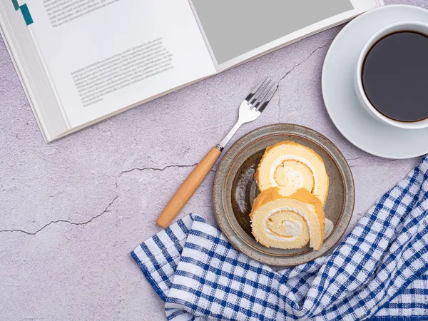 Top view of a book with roll cakes on a plate, a white coffee cup, and a cloth placed on a gray stone background. Space for text. Concept of relaxation.