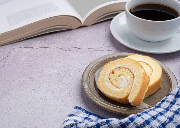 Top view of a book with roll cakes on a plate, a white coffee cup, and a cloth placed on a gray stone background. Space for text. Concept of relaxation.