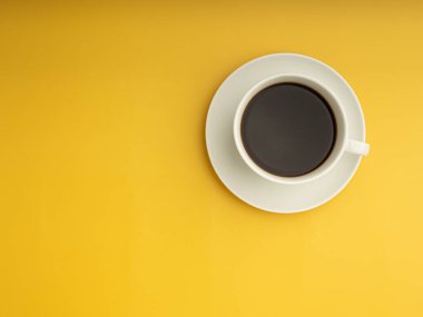 Beyaz bir kahve fincanının üst görüntüsü sarı bir fonda yer alır. Mesaj için yer var. İçecek ve rahatlama kavramı.