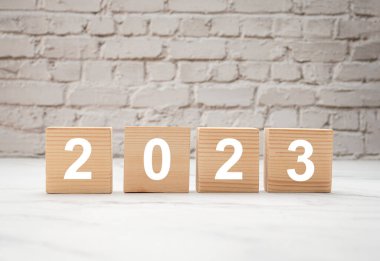 2023 'e gidiyoruz. Beyaz tuğlalı arka planda 2023 harfli tahta küpler. Üst Manzara. Yeni yıl arifesi ve 2022 'yi 2023' e değiştirmek.
