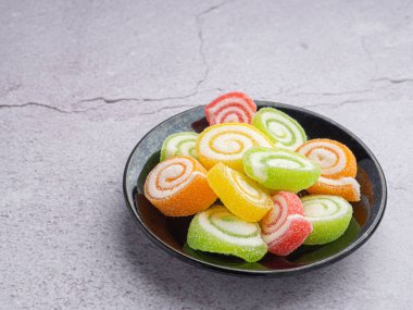 Siyah bir tabakta, gri taştan bir arka planda duran renkli, tatlı bir jöle şekeri. Şekerli jöle çemberi. Metin için kopyalama alanı olan yan görünüm. Çocuklar için tatlı kavramı.