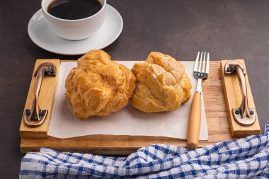 Ahşap bir tepside koux krema ve koyu arkaplanda beyaz bir kahve fincanı. Mesaj için yer var. Rahatlama kavramı.