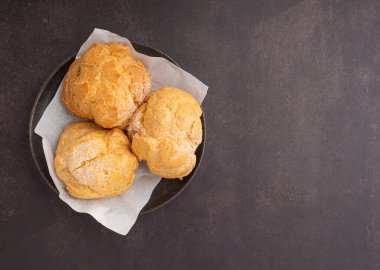 Koyu kahverengi arkaplana yerleştirilmiş bir tabaktaki choux kreminin üst görüntüsü. Mesaj için yer var. Mesaj için yer var. Rahatlama kavramı.
