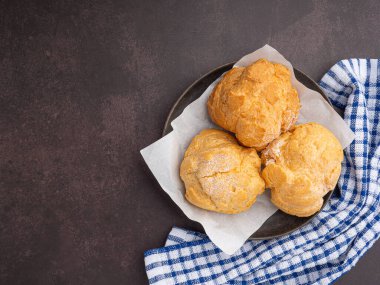 Tabaktaki choux kremi ve koyu kahverengi arka plandaki kumaş manzarası. Mesaj için yer var. Rahatlama kavramı.