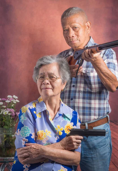 Portrait of an elderly couple holding a shotgun and a sport air rifle while sitting and standing with a vintage background. Pneumatic gun. Concept of aged people and sport..