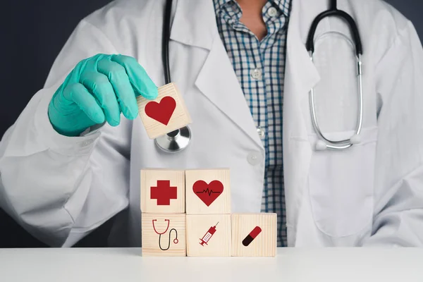 A doctor holding wooden dice with icons of health and doctor. Close-up photo. Space for text. Concept of doctor and healthcare.