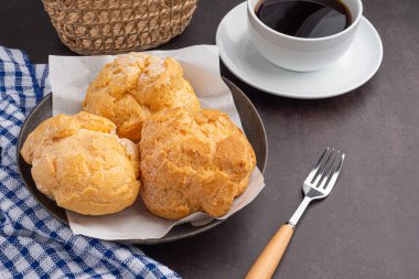 Top view of choux cream on a plate and a white coffee cup with a cloth placed on the old kitchen table. Space for text. Concept of dessert, beverage, and relaxation.