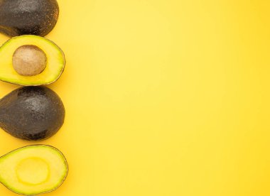 Top view of the fresh avocado whole and half placed on a yellow background. Organic fruit. Space for text. Concept of healthy fruits and healthcare.