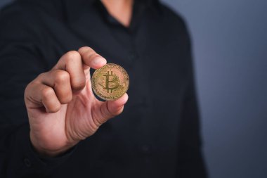 Yatırımcı adam, koyu gri arka planı olan bir Bitcoin altın para gösteriyor. Yakın plan fotoğraf. Mesaj için yer var. Sanal kripto para birimi ve gelecekteki para kavramı.