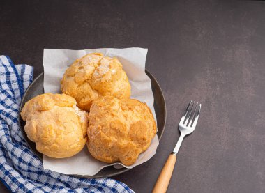 Tabaktaki choux kremi ve masadaki kumaş manzarası. Mesaj için yer var. Tatlı ve rahatlama kavramı.