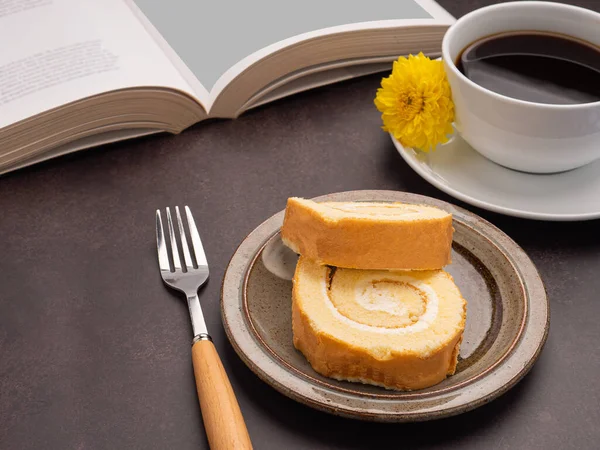 Top view of a book with roll cakes on a plate, a white coffee cup, and a cloth on a table. Space for text. Concept of reading and relaxation.