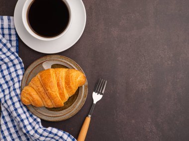 Tabakta bir kruvasan ve masada bir bez ve çatal bıçak ile beyaz bir kahve fincanı. Mesaj için yer var. Rahatlama kavramı.