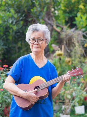 Kısa gri saçlı, gülümseyen, gitar çalan ve bahçede dikilirken kameraya bakan yaşlı bir kadının portresi. Emekli olduktan sonra hayatın tadını çıkar. Yaşlılar ve rahatlama kavramı.