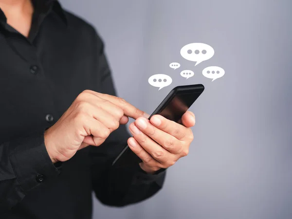 Businessman using a smartphone with an conversation icon while standing with a gray background. Space for text. Communication and technology concept.