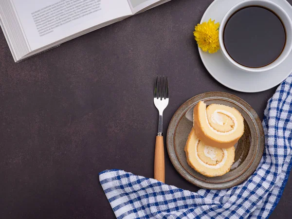 Top view of a book with roll cakes on a plate, a white coffee cup, and a cloth on a table. Space for text. Concept of relaxation.
