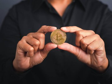 Gri arka planı olan bir iş adamı elinde bitcoin para tutarken siyah gömlek giyiyor. Yakın plan fotoğraf. Mesaj için yer var. Sanal kripto para birimi ve gelecekteki para kavramı.