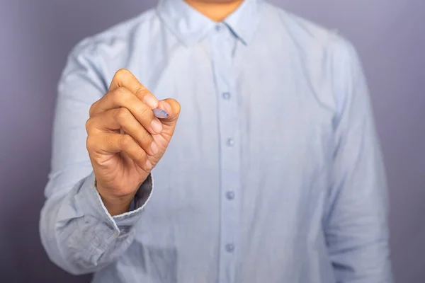 stock image A businesswoman wearing a light blue shirt is holding a pen write or writing on the virtual screen or in the air against a gray background. Space for text. Modern business background concept.