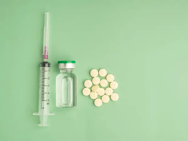 stock image Pile of medicine tablets, a vaccine bottle, and syringe on a light green background. Flat lay. Top view. Space for text. Medicine and treatment concept.