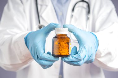 Mavi eldivenli bir doktorun elinde ve hastanede dururken ilaç şişesi tutuyor. Tıbbi, sağlık ve tedavi kavramı.