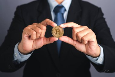 Gri bir arka planda dururken Bitcoin altın sikke gösteren bir işadamı eli. Yakın plan fotoğraf. Mesaj için yer var. Sanal kripto para birimi ve gelecekteki para kavramı.