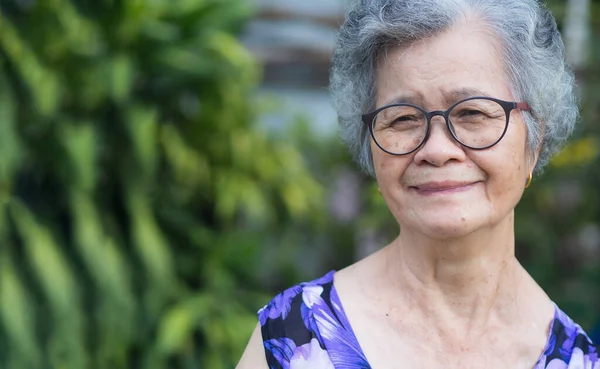 Portrait of a senior woman with short white hair looking at the camera with a smile while standing in the garden. Aged people and health care concept