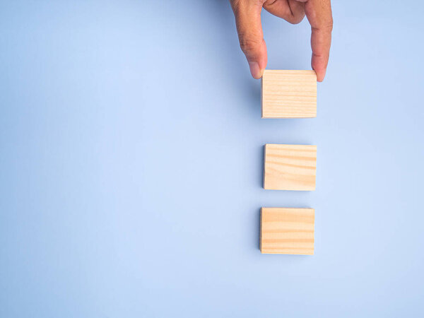 Close-up of hand holding empty wooden blocks on a light blue background. Space for text.