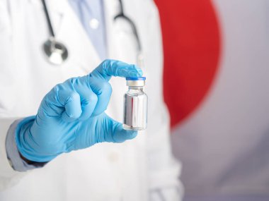 Elinde aşı şişesi tutan doktor Japon bayrağının arka planına karşı aşı hazırlıyor. Bağışıklık aşısı ve virüs enfeksiyonuna karşı tedavi. Tıbbi konsept.