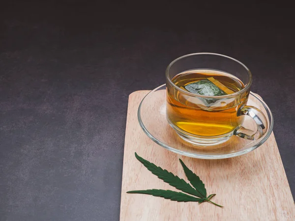 A cup of hemp tea and marijuana leaf laid on a wooden cutting board with a vintage background. Cannabis herbal tea. Close-up photo. Selective focus. Relaxation concept.