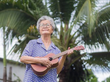 Kısa gri saçlı, ukulele çalan ve bahçede dikilirken kafasını kaldıran son sınıf bir kadının portresi. Emekli olduktan sonra hayatın tadını çıkar. Yaşlılar ve rahatlama kavramı.