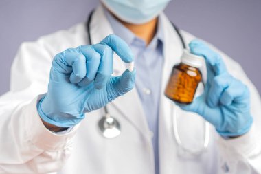 Yüz maskesi takan bir doktor, mavi eldiven giyen bir el, ve hastanede dururken ilaç ve ilaç şişesi tutan bir doktor. Sağlık ve Tıp Konsepti.