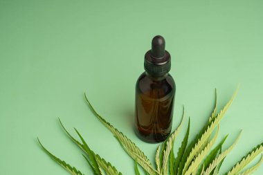 Şişede özüt yağı ve yeşil arka planda marihuana yaprakları olan tıbbi esrar..