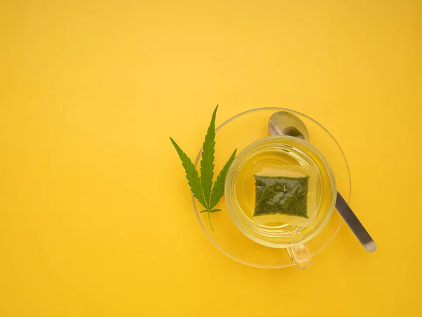 A cup of hemp tea laid isolated on a yellow background. Cannabis herbal tea. Close-up photo. Top view. Flat lay. Space for text. Relaxation concept.