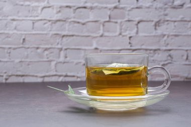 Beyaz tuğlalı bir arka planda bir fincan kenevir çayı. Kenevir bitki çayı. Yakın plan fotoğraf. Seçici odaklanma. Sağlıklı içecek ve rahatlama kavramı.