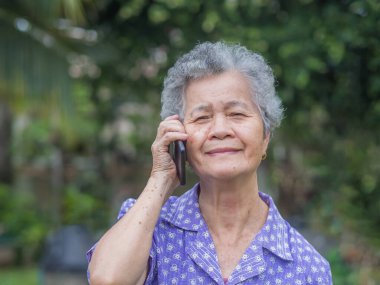 Mutlu, güzel, son sınıf öğrencisi bir kadın akıllı telefon kullanıyor, gülümsüyor ve bahçede dikilirken kameraya bakıyor. Mesaj için yer var. Yaşlılar ve iletişim konsepti.