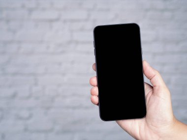 Beyaz tuğlalı arka planı olan bir akıllı telefonun el ele tutuşması. Yakın plan fotoğraf. Mesaj için yer var. Teknoloji ve iletişim konsepti.