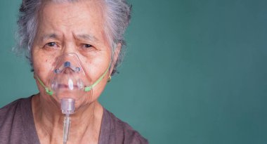 Tıbbi solunum maskesi takan yaşlı bir Asyalı kadının yakın çekimi. Oksijen maskesi takan hasta yaşlı kadın zatürree koronavirüs salgını ve tedavi görüyor..