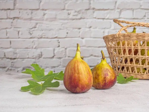 Figs fruit and leaves are on a cement floor with a bamboo basket and white brick wall background. High Vitamins fruit. Space for text. Healthy fruits and healthcare concept.