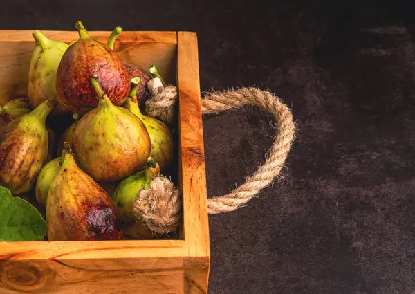 Ripe figs fruit are in a wooden crate on the old table in the kitchen. Top view. Space for text. Close-up photo. Healthy fruits concept.