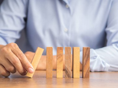 Yakın plan, tahta bir bloğu domino taşına bastır. İş konseptinde risk ve strateji.