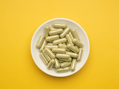 Andrographis 'in panikleme kapsülleri sarı arka planda izole bir kapta. Mesaj için yer var. Bitkisel, ilaç ve sağlık hizmetleri kavramı.